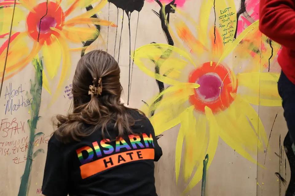 A Team Enough member wearing a Brady disarm hate t shirt signs a mural in honor of victims of gun violence
