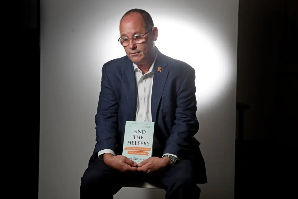 Fred Guttenberg poses with his book find the helpers with an orange ribbon for jaime