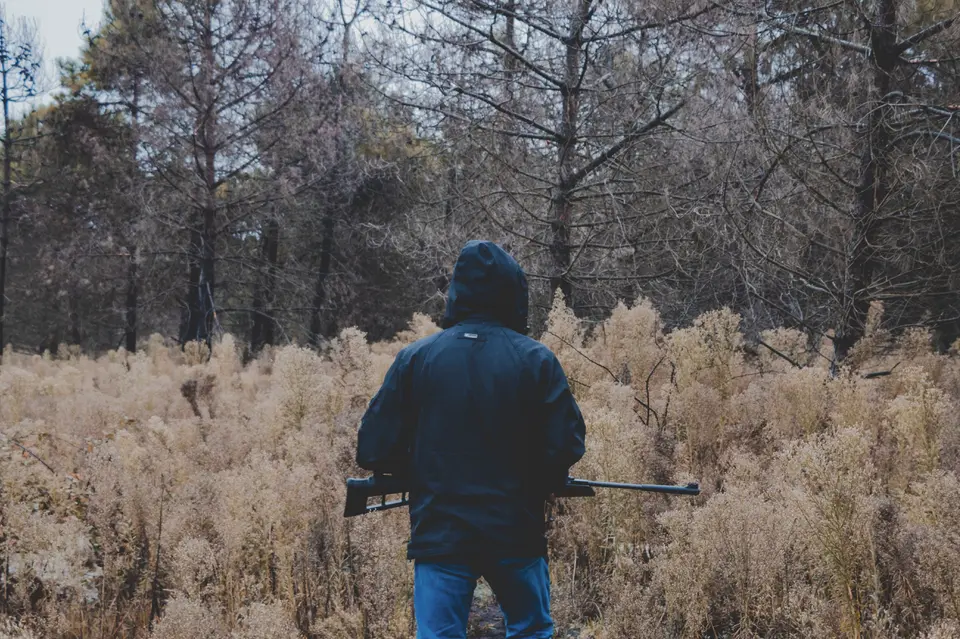 Hunter stands in rural field with shotgun