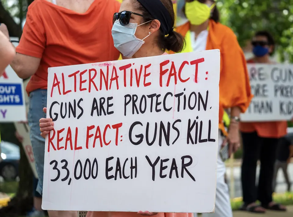 Woman stands at a protest at nra headquaters with a sign reading alternative fact